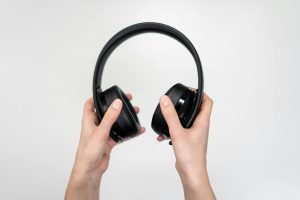 Close-up of hands holding black wireless headphones against a white background.